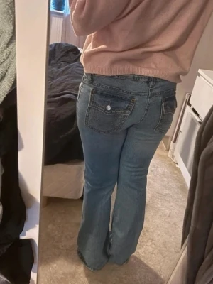 Blå bootcut jeans med slitningar - Säljer ett par blå bootcut jeans med snygga slitningar på knäna och klassiska femficksdetaljer. Lappen har tagits av men aldrig använda 