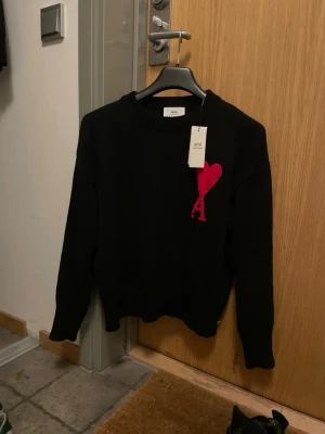 Ami Paris sweater - Svart stickad tröja från Ami Paris med ett stort rött hjärta och bokstaven A broderat på bröstet. Tröjan har rund hals, ribbade muddar och lång ärm. Har använt i några månader men den är fortfarande i nyskick👌🏾
