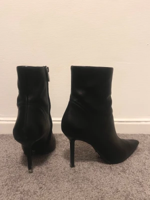 Svarta stövletter med smal klack - Säljer ett par svarta stövletter från Saint Laurent i mjukt skinn med spetsig tå och smal hög klack. Snygg siluett och dragkedja på sidan för enkel på- och avtagning. Perfekta för dig som gillar stilrena boots med edge.