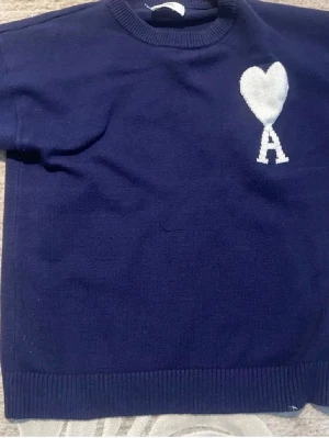 Mörkblå stickad tröja från Ami - Snygg mörkblå stickad tröja från Ami Alexandre Mattiussi med vit hjärtdetalj och bokstaven A på bröstet. Tröjan har rund hals, ribbade muddar och lång ärm. Perfekt för dig som gillar stilrena plagg med en twist.
