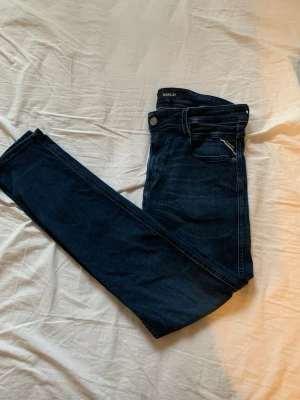 Replay mörkblå jeans, storlek 30/32 - Snygga mörkblå jeans från Replay med klassisk femficksdesign och diskreta slitningar. Modellen har normal passform och raka ben, perfekt för dig som gillar stilrena och tidlösa jeans. Materialet är mjukt och följsamt denim.
