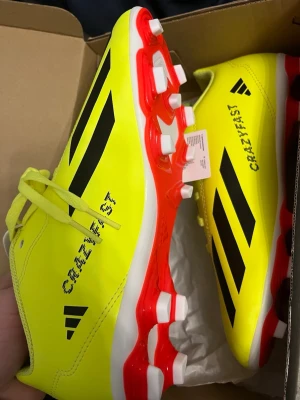 Adidas X Crazyfast Club FxG fotbollsskor - Säljer ett par Adidas X Crazyfast Club FxG fotbollsskor i storlek 38. Skorna är knallgula med svarta Adidas-ränder och har röda och vita dobbar. De har snörning och är tillverkade i syntetmaterial, perfekta för gräsplan. Modellen är riktigt lätt och har en sportig vibe.NYA OCH OTESTADE