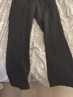 Svarta kostymbyxor med rak passform - Snygga svarta kostymbyxor med rak passform och klassisk look. Perfekta för dig som vill ha en stilren och enkel byxa till garderoben. Materialet känns mjukt och har en lätt glans, vilket ger en dressad känsla. Passar till skjorta eller t-shirt beroende på humör