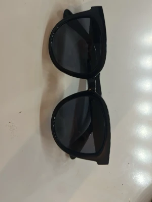Solglasögon (helt nya från en butik utomlands)  - Bilderna visar ett par svarta solglasögon med breda bågar och mörka glas, ingen väst syns på bilderna. 