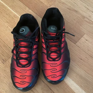 Nike Air Max Plus röd/svart sneakers - Nike Air Max Plus sneakers i rött och svart med coola vågformade detaljer och svart sula. Skorna har synlig Air-dämpning, svarta snören och en liten silverfärgad Swoosh på sidan. Ovandelen är i syntetmaterial och mesh för en sportig vibe. Köpta för 2500 seljer för 1700 använda ca 5 gånger tvättas såklart innan 🩷