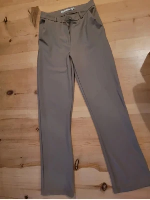 Beige kostymbyxor från 157 XS - Snygga beige kostymbyxor från 157 i storlek XS. Byxorna har raka ben, bälteshällor och stängs med knapp och dragkedja. Perfekta för en clean och stilren look. Materialet känns mjukt och har en lätt stretch för extra komfort. Använd vid ett tillfälle. 