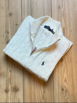 Vit stickad half zip-tröja Polo Ralph Lauren M - Säljer en vit stickad tröja från Polo Ralph Lauren med half zip och klassisk kabelstickad design. Tröjan kommer inte med stags eftersom min mamma tog av den och hon trodde att jag skulle ha den på mig