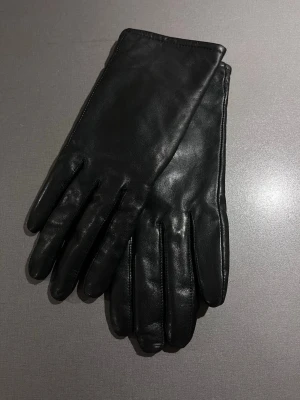 Svarta skinnhandskar med klassisk look - Läckra stilrena skinnhandskar i polerat skinn. Foder invändigt. Onesize men passar ringstorlek 16 som handen i handsken 😊 Mycket bra skick, som nya! Säljs på flera sidor, först till kvarn. 