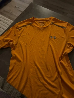 T-shirt  - Bilden visar en orange t-shirt från Under Armour, inte en sko. Vänligen ladda upp en bild på skor för att få en relevant beskrivning.