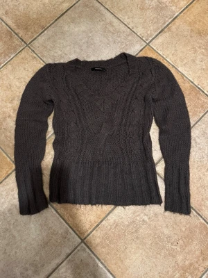Mörkgrå stickad tröja Vero Moda - Mysig mörkgrå stickad tröja från Vero Moda i storlek M. Tröjan har ett grovt kabelstickat mönster framtill, v-ringad hals och långa ärmar. Perfekt för kyliga dagar och enkel att matcha med jeans eller kjol.