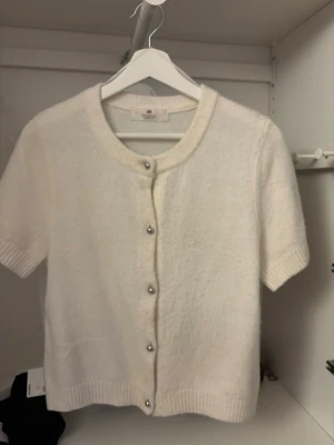 Vit kortärmad kofta från H&M - Kortärmad kofta från H&M. Rund halsringning, ribbade kanter och silvriga knappar framtill. Perfekt att slänga över ett linne.