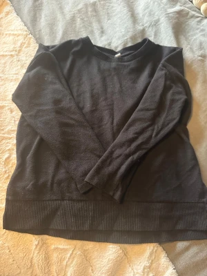 Svart stickad tröja från Hons - Svart stickad tröja från Hons i storlek S. Tröjan har rund hals, långa ärmar och breda ribbade muddar vid nederkant och hals. Perfekt för lager-på-lager och chill dagar. Enkel och stilren design som funkar till många outfits.