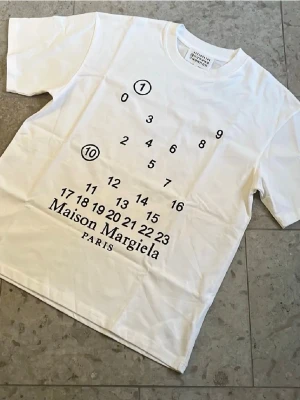 Vit Maison Margiela tshirt - Vit t-shirt från MM6 med ikoniskt svart sifferprint och logga på bröstet. Storlek M och oanvänt skick, fraktar inom 24h✅ vid mer frågor hör bara av er🏌️