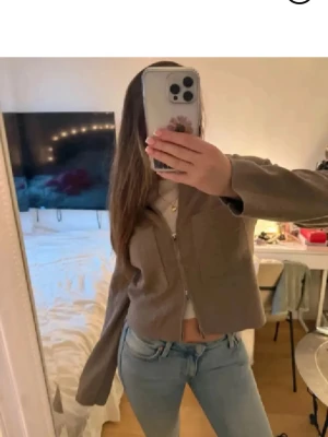 Beige croppad overshirt med dragkedja - Snygg beige croppad overshirt från Åhlens med två stora fickor framtill och dragkedja. Jackan har klassisk krage och raka, långärmade ärmar. Materialet är stickad ullmix som känns mjuk och skön mot huden. Perfekt för lager-på-lager och chill stil. Köpt 699 kr . Har även i vit på annan annons