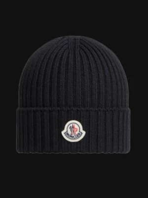 Svart ribbad Moncler mössa - Säljer en svart ribbstickad mössa från Moncler med uppvikt kant och klassisk logotyp framtill. Mössan är enkel men stilren och passar perfekt för kalla dagar. Materialet är mjukt och håller värmen bra.