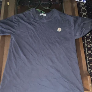 Blå Moncler t-shirt med logga - Snygg blå t-shirt från Moncler med klassisk rund hals och korta ärmar. På bröstet sitter Monclers ikoniska logga i vitt och rött. T-shirten är gjord i mjuk bomull och har en clean, stilren look som funkar till allt.