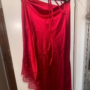 Rött nattlinne med spets - Röd nattlinne i silkes material & spets med slits på benet & spetsdetaljer. Har tunna axelband som knyts i nacken.