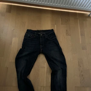 Mörkblå jeans från Nudie Jeans, W29 L32 - Snygga mörkblå jeans från Nudie Jeans med klassisk femficksdesign och kontrastsömmar. Jeansen har rak passform och är tillverkade i slitstarkt bomullsjeans. Perfekta för dig som gillar stilrena och tidlösa jeans.