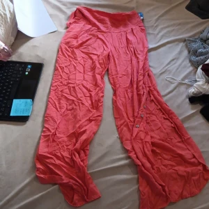 Röda vida linnebyxor från Cantik - Snygga vida linnebyxor i en härlig röd färg från Cantik. Byxorna har hög midja, knappar längs bena. Perfekta för varma dagar när du vill ha en luftig och chill stil. Stretch resår på baksidan