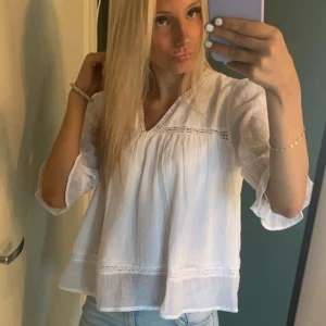 Vit blus från Gina Tricot med spetsdetaljer - Säljer en luftig vit blus från Gina Tricot i storlek 170. Blusen har v-ringning, spetsdetaljer och volang vid ärmslut. Den är tillverkad i tunn bomull och har en loose passform. Mycket fin att kombinera med en loose-stickad kofta! Endast använd en gång och har inga defekter💞