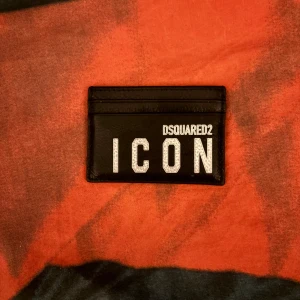 Svart korthållare DSQUARED2 ICON - Snygg svart korthållare från DSQUARED2 med stor vit 'ICON'-text på framsidan. Tillverkad i äkta skinn och har flera kortfack. Perfekt för dig som vill ha en stilren och trendig accessoar i fickan. Den är perfekt storlek och du får med dig den överallt!😁😁Nypris cirka 1200-1800