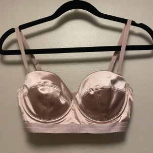 Champagnefärgad korsett från Lounge - Snygg champagnefärgad korsett-topp från Lounge i glansigt satinliknande material. Toppen har justerbara axelband och bred resår med Lounge-logga. Perfekt för att lyfta din outfit med en lyxig touch.