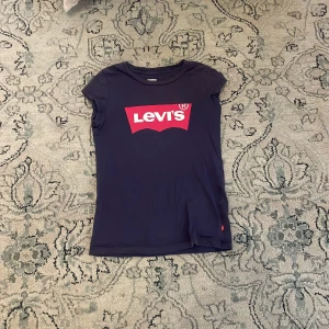Mörkblå Levi's t-shirt med logga - Snygg mörkblå t-shirt från Levi's med klassisk röd och vit logga framtill. T-shirten är kortärmad och har en feminin passform. Tillverkad i mjuk bomull som är skön att ha på sig hela dagen. Storlek 140 men själv tycker jag den passar som 146/152. Säljer för jag inte använder den🥰