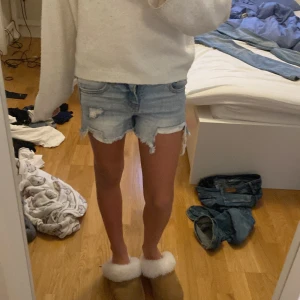 Ljusblå jeansshorts - Säljer ett par ljusblå jeansshorts från art class med råa, fransiga kanter och slitna detaljer. Klassisk femficksmodell med normal passform och knapp- och dragkedjestängning. Perfekta för varma dagar och enkel att matcha med allt.