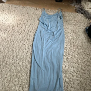 Ljusblå långklänning med smala axelband - Säljer en ljusblå långklänning med smala axelband och rak passform. Klänningen har en enkel och stilren design, perfekt för dig som gillar minimalistiska vibes. Materialet känns mjukt och svalt, vilket gör den skön att bära under varmare dagar.