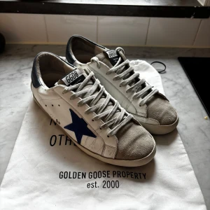 Golden Goose skor(kom med prisförslag) - (Kom med prisförslag ) Säljer ett par klassiska Golden Goose-sneakers i storlek 42. Skorna är använda men i bra skick och har den typiska “distressed looken” som märket är känt för.  ✔️ Äkta Golden Goose ✔️ Original dustbag medföljer (se bild 5) ✔️ Bekväma och stilrena – passar både till vardag och mer uppklätt  Notera: På sulorna finns två små defekter/slitningar (se bilder), men inget som påverkar användning eller komfort.  Nypris ca 4 000–5 000 kr.  Mitt pris: 2299