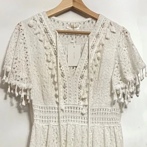 Vit spetsklänning från MC Lorene - storlek M/L - Superfin långklänning i vit spets från MC Lorene. Klänningen har korta ärmar med tofsdetaljer, v-ringad hals och snygga virkade partier. Materialet är bomull och spetsen har ett blommigt mönster. Perfekt för sommarens alla tillfällen!