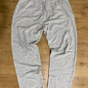 Grå mjukisbyxor från 157, storlek L - Grå mjukisbyxor från 157 i storlek L. Byxorna har resår och snörning i midjan för skön passform. Tillverkade i mjukt material med borstad insida som känns riktigt bekväm. Perfekta för chill eller träning.