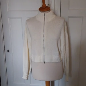 Vit stickad kofta från H&M Divided - Säljer en vit stickad kofta från H&M Divided i storlek M. Koftan har hög krage, hel dragkedja framtill och ribbade muddar vid ärmslut och nederkant. Perfekt för lager-på-lager och chill stil.