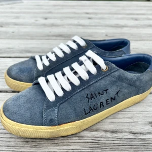 Saint Laurent blå mocka sneakers - Snygga blå sneakers i utmärkt skick från Saint Laurent i mocka med handskriven logga på sidan. Skorna har vita snören, beige sula och rund tå. Insidan är fodrad i blått läder för extra komfort. Perfekta för dig som gillar en stilren men ändå unik look. Skorna är mycket ovanliga.