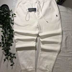 Vita mjukisbyxor från Polo Ralph Lauren - Snygga vita mjukisbyxor från Polo Ralph Lauren med broderad logga på benet. Byxorna har dragsko i midjan, muddar vid bensluten och en bakficka. Perfekta för en chill och stilren look.