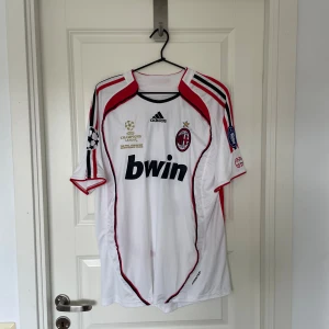 AC Milan Maldini Champions League tröja - AC Milan fotbollströja från Adidas, Champions League-final edition med Maldini och nummer 3 på ryggen. Vit med röda och svarta detaljer, broderat klubbmärke och Champions League-patch på ärmen. Tillverkad i lätt polyester, perfekt för fans och samlare.