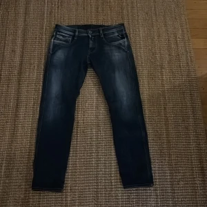 Replay Anbass jeans i mörkblå denim - Säljer ett par Replay Anbass jeans i mörkblå tvätt med snygga slitningar. Modellen har smal passform och klassiska fem fickor. Jeansen är tillverkade i stretchig denim för extra komfort och har en modern look som passar till det mesta.