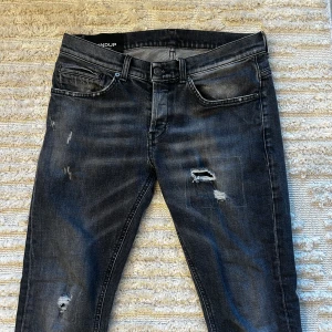 Mörk grå Dondup George  - Säljer ett par gråa Dondups med slitna detaljer. Strlk 31. Modellen är 181cm och de passar sjukt bra. Sjukt snygga jeans för en lite mer uppklädd vardag men funkar även för fest. Har fixat 2 hål på dem hos en skräddare, fråga om bild om du vill se.