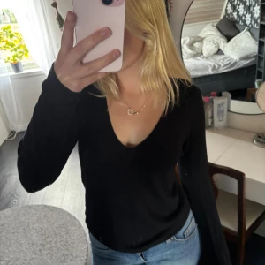 Svart v-ringad långärmad tröja - En svart långärmad tröja med djup v-ringning. Tröjan har en enkel och stilren design som passar perfekt till jeans. Mjuk och skön att bära, med normal passform och klassisk look.