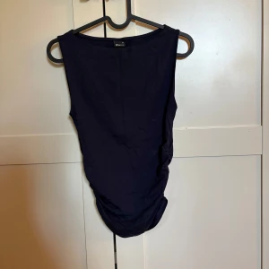 Mörkblå topp  - Säljer en mörkblå topp. Toppen har en tight passform och snygg rynkdetalj längs sidorna. Materialet känns mjukt och stretchigt.