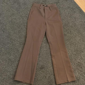 Bruna bootcut kostymbyxor  - Snygga bruna kostymbyxor med bootcut-ben och hög midja. Byxorna har klassiska fickor fram, hällor för bälte och stängs med dragkedja och knapp. Perfekta för en clean och stilren look. Fick inte till baksidan så snyggt. Jag är också 1,55 cm perfekt längd och bara använts fåtal gånger.