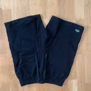 Svarta Lacoste Shorts - Svarta shorts från Lacoste med klassisk krokodil-logga på benet. Regular fit med elastisk midja och snörning för skön passform. Tillverkade i mjuk bomull, perfekta för chill dagar eller träning. En bakficka och enkel design gör dem riktigt användbara.