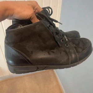 Svarta kängor i skinn och mocka - Svarta kängor med både skinn- och mockadetaljer, snörning framtill och dragkedja på sidan för enkel påtagning. Snyggt robust sula och rund tå, perfekt för dig som gillar en stilren och enkel look.