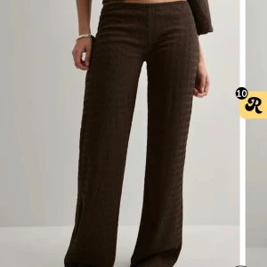 Bruna vida byxor med struktur - Snygga bruna byxor med vid passform och strukturerat tyg. Byxorna har låg midja och raka ben, perfekta för en trendig och avslappnad look. Passar till både sneakers och klackar. Nyskick, med prislapp kvar.