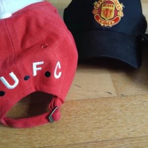 3 st 200 kr st Manchester United kepsar i bomull - Två klassiska Manchester United kepsar i bomull, en i svart med broderat klubbmärke och en i rött och vitt med Premier League-logga och U.F.C-tryck baktill. Justerbar rem baktill för perfekt passform. Perfekt för dig som vill visa ditt lagstöd.