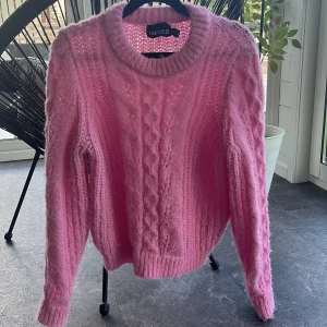 Rosa stickad tröja från Pieces - Supermysig rosa stickad tröja från Pieces i storlek XS. Tröjan har ett snyggt flätmönster framtill, ribbade muddar och är långärmad. Perfekt för dig som gillar en fluffig och trendig look med lite oversized känsla. Men den är lite nopprig