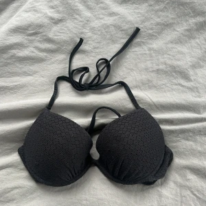 Svart bikiniöverdel med knyt - Snygg svart bikiniöverdel med vadderade kupor och knyt i nacken. Ytan har ett diskret hålmönster som ger en extra touch. Perfekt för stranden eller poolen, enkel att matcha med olika underdelar då den är svart o basic 💓