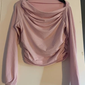Ljusrosa draperad långärmad topp - Säljer en ljusrosa långärmad topp med snygga draperingar och rynkade detaljer på sidorna. Toppen har en bred, lös halsringning som ger en cool och avslappnad vibe. Perfekt att styla med jeans eller kjol för en trendig look.