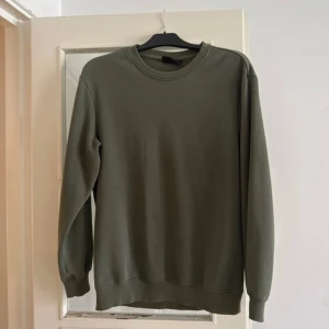 Olivgrön sweatshirt från H&M - En olivgrön crewneck sweatshirt från H&M i relaxed fit. Tröjan har rund halsringning, långa ärmar och är tillverkad i mjuk bomullsblandning. Perfekt för en chill och enkel stil.