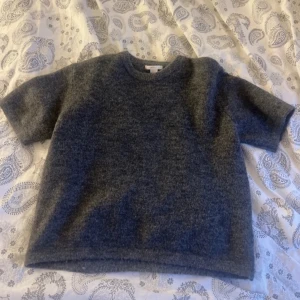 Mörkgrå ulltröja med kort ärm - Mysig mörkgrå tröja i ull med korta ärmar och rund hals. Perfekt för lager-på-lager och passar till både jeans och kjol. Enkel och stilren design som funkar året runt. Storlek 158/164 men sitter som en xxs/xs